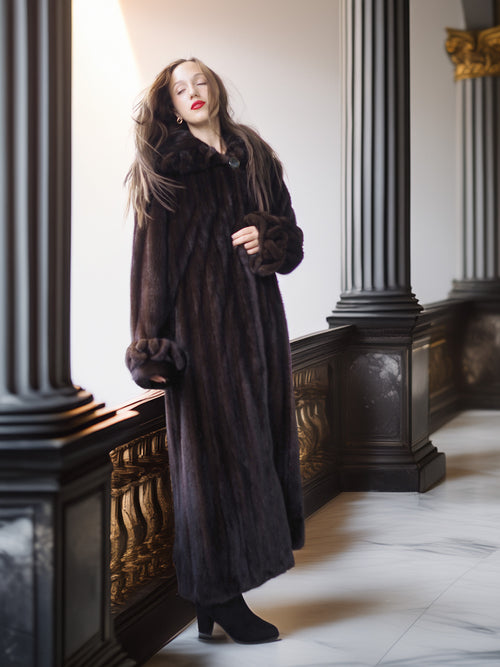 Woman wearing a long dark fur coat in an elegant interior setting.