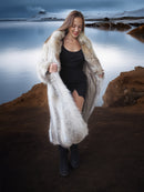 Woman in a fur coat standing in a rugged landscape with a lake.