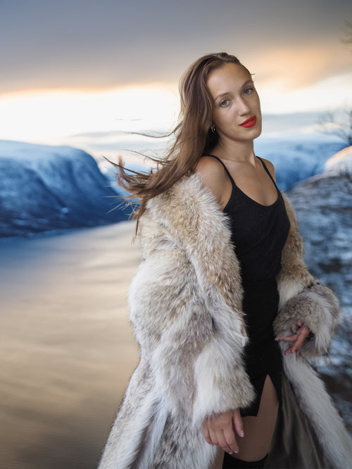Woman in a fur coat standing in a snowy landscape with mountains in the background