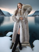 Woman in a fur coat standing on a snowy platform with a scenic lake and mountains in the background