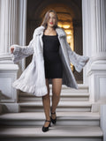 Woman in a long gray fur coat standing on steps in an elegant interior setting