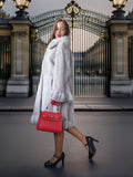 Woman in a fur coat holding a red handbag in front of an ornate gate.