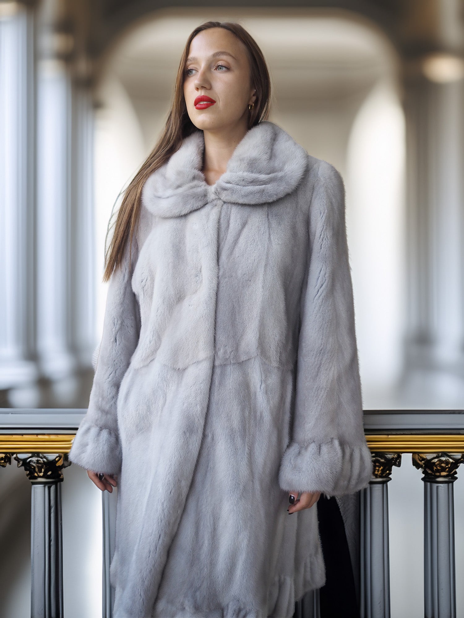Woman wearing a gray fur coat standing indoors with a blurred background