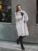 Model poses playfully in Sapphire Grey Mink Fur Coat S Petit Excellent against a modern textured wall, blending vintage and contemporary style.