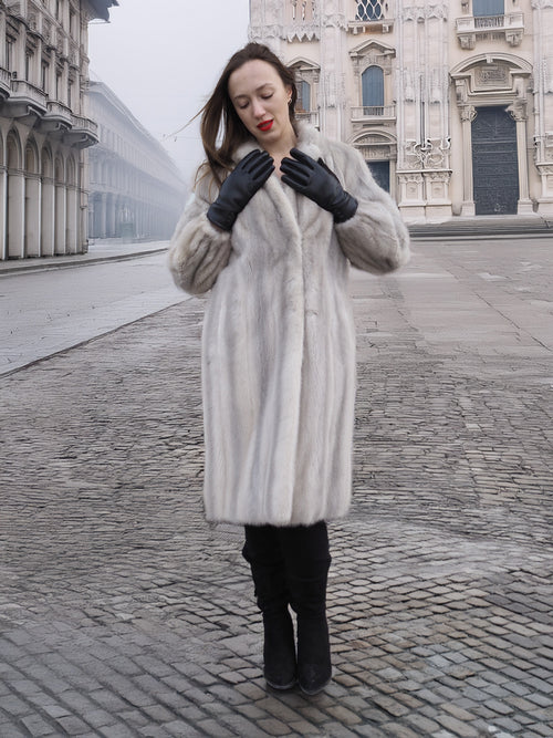 Model adjusts gloves while wearing Sapphire Grey Mink Fur Coat S Petit Excellent, ideal for sustainable and elegant winter fashion.