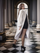 Woman in a white fur coat standing in an elegant interior setting with checkered floor.
