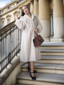 Woman in a white fur coat standing on steps with a brown handbag