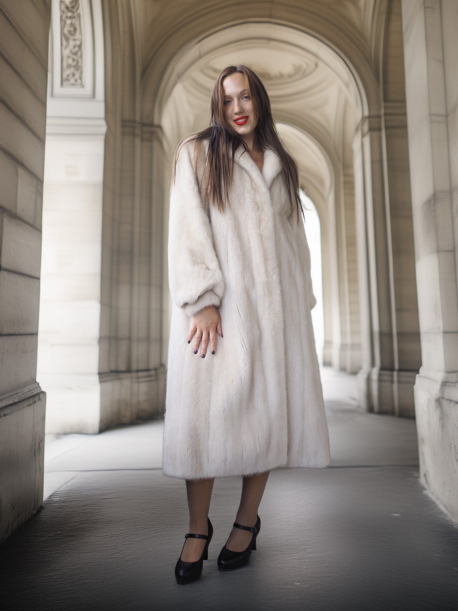 Woman in a long white coat standing in an archway with classical architecture.