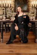 Woman in a black outfit sitting on a chair in a formal setting with candles and a stone wall.