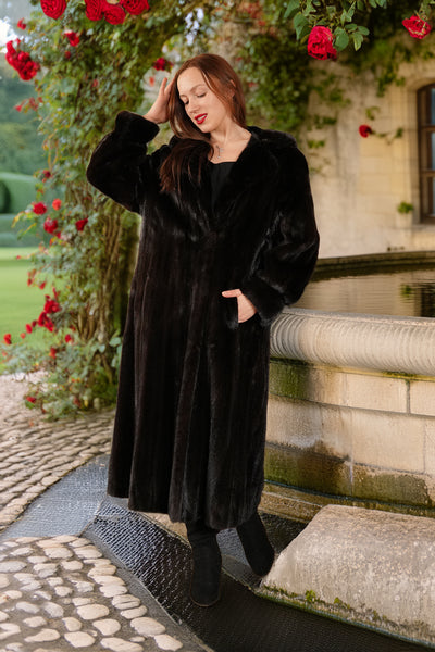 Woman in a black coat standing on stone steps with red flowers and a building in the background