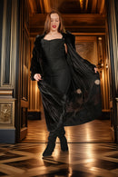 Woman in a black coat and dress standing in an elegant interior setting