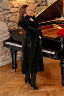 Woman in a black fur coat standing next to a grand piano with red flowers on a stone wall background