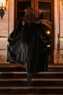 Person wearing a long black coat walking up steps at night.