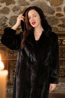 Woman wearing a black fur coat in front of a stone wall.