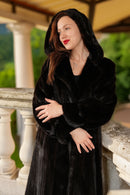 Woman wearing a black fur coat on a balcony with greenery in the background