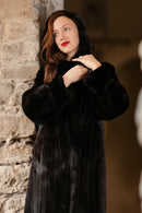 Woman wearing a black fur coat against a stone wall.