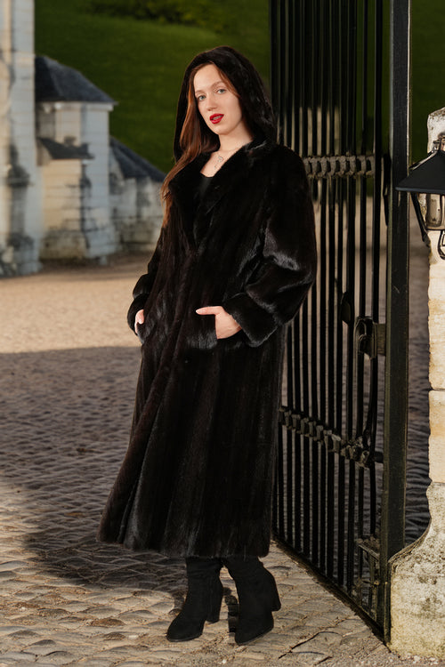 Woman in a long black coat standing in front of a black metal gate.