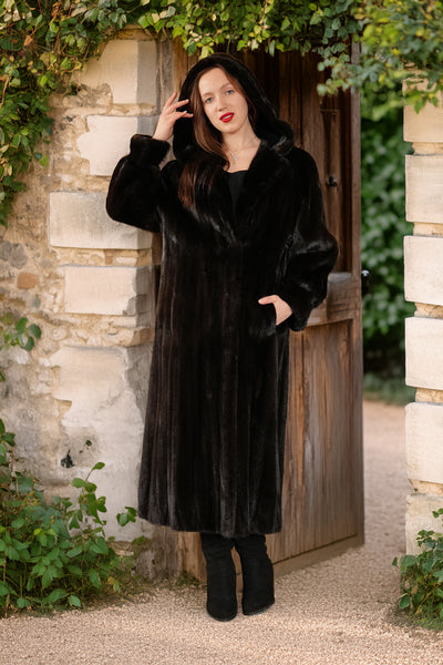 Woman wearing a black fur coat standing in front of a stone wall and wooden door.
