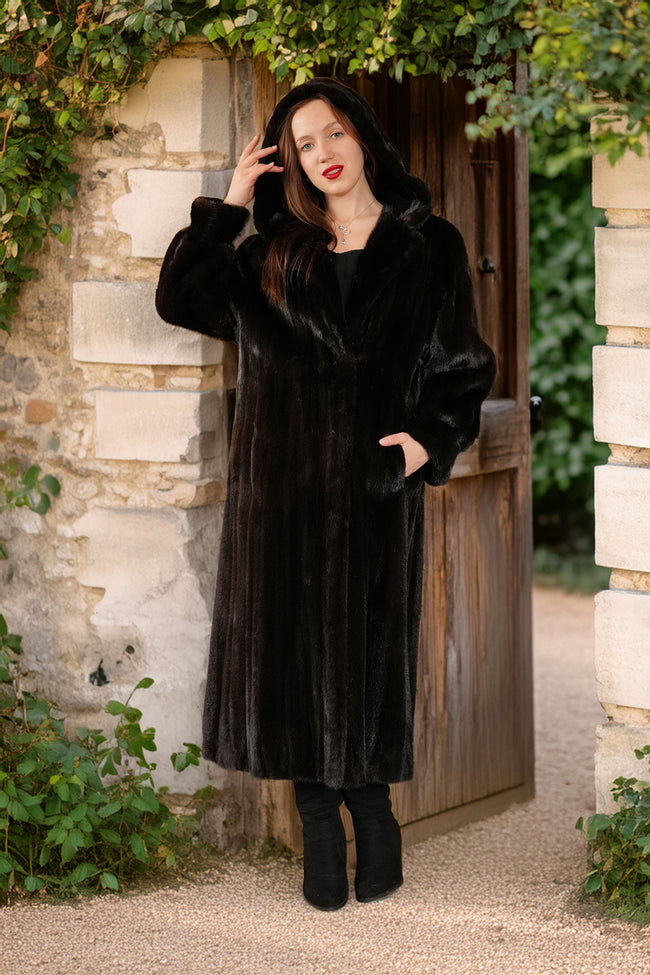 Woman wearing a black fur coat standing in front of a stone wall and wooden door.