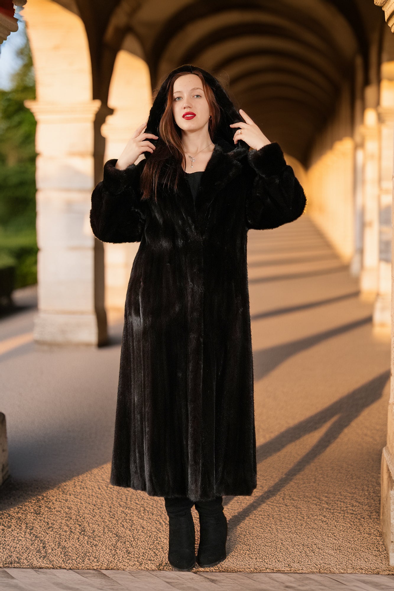Woman wearing a black coat standing under an archway with warm lighting.