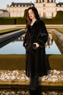 Woman in a black coat standing in front of a large building with a reflective pool.