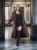 Woman wearing a long brown fur coat and black knee-high boots in an elegant interior setting.