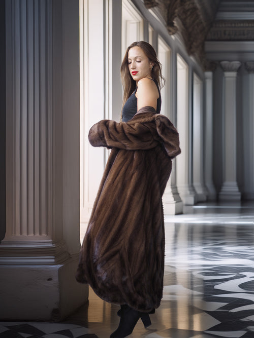 Woman in a long fur coat standing in an elegant hallway with columns.