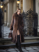 Woman in a fur coat standing in front of an ornate gate.