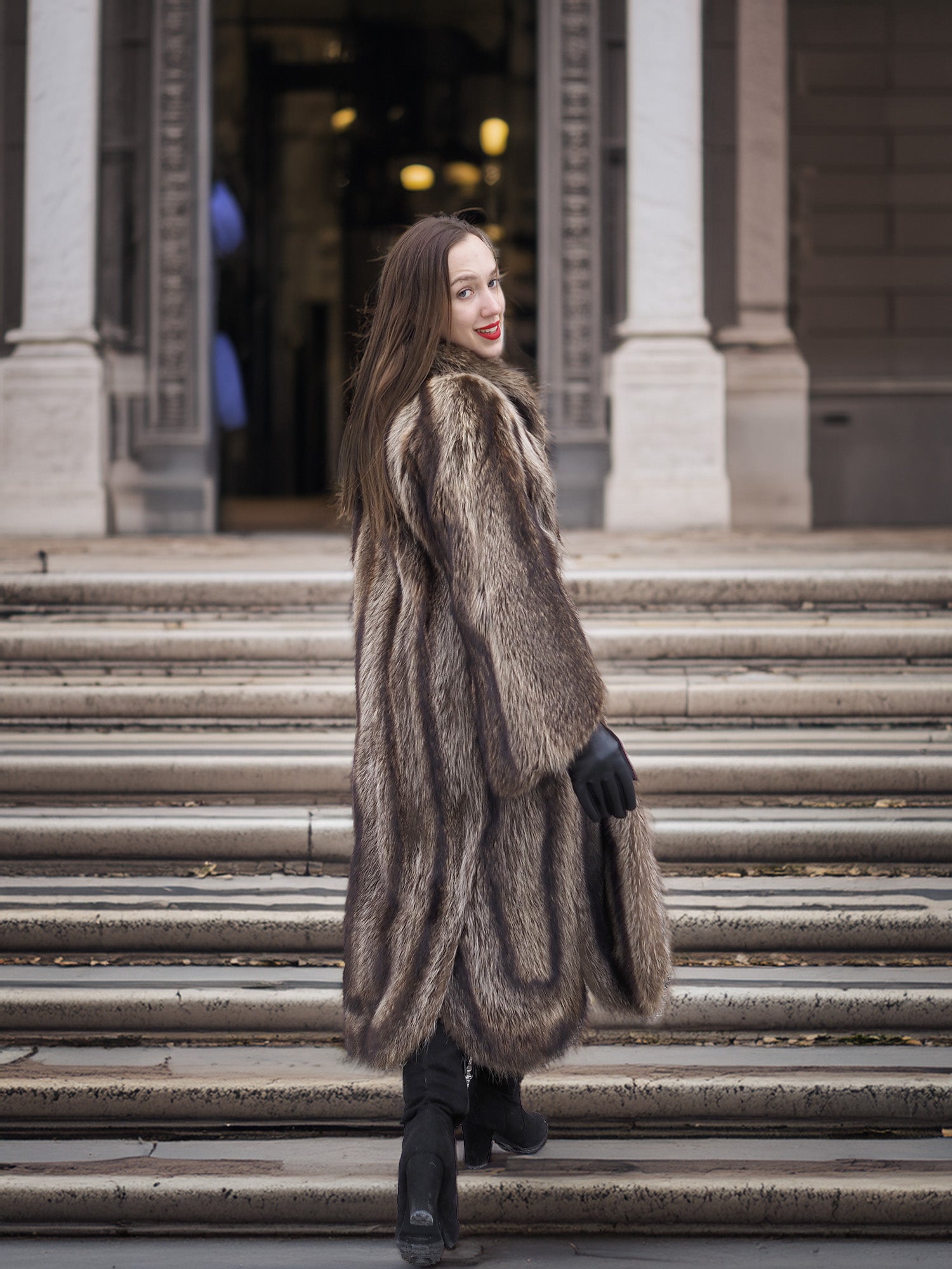 Back view of Canadian Raccoon Fur Coat in silver tips on stairs, highlighting full-length design and elegant winter outerwear.