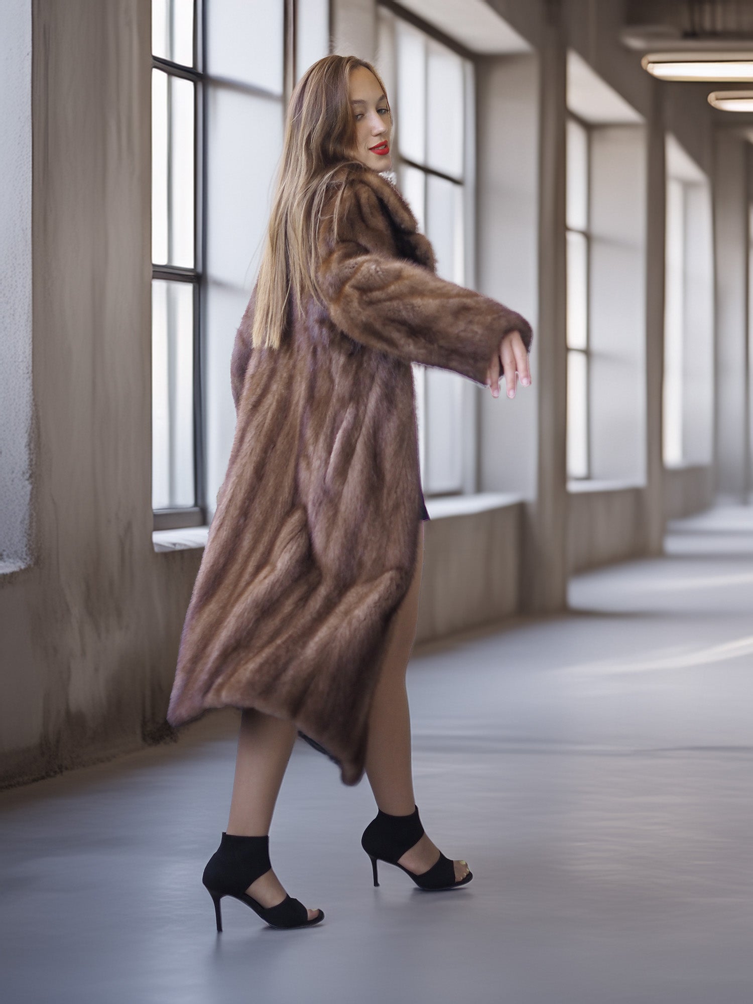 Woman wearing a long brown fur coat in a modern building hallway.