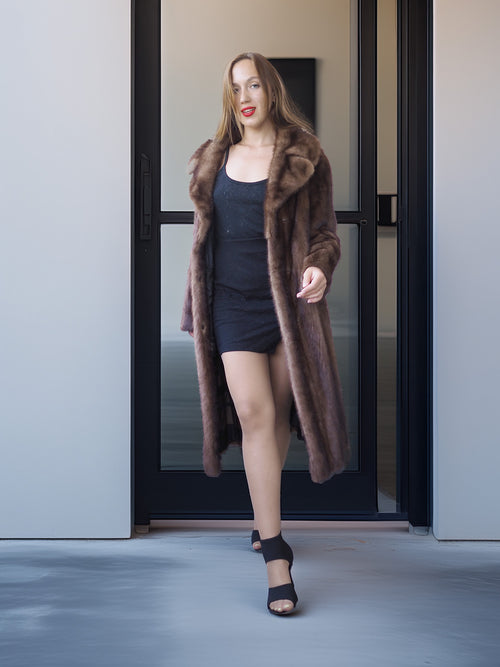 Woman wearing a long brown fur coat standing in front of a glass door.