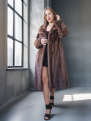 Woman wearing a long brown fur coat in a modern interior setting.