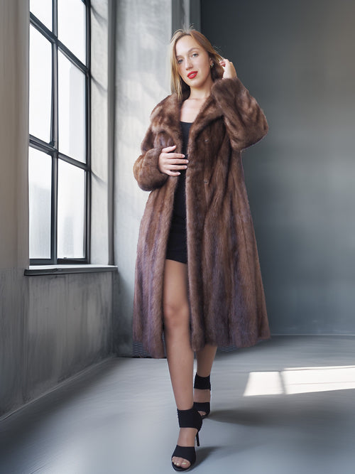 Woman wearing a long brown fur coat in a modern interior setting.