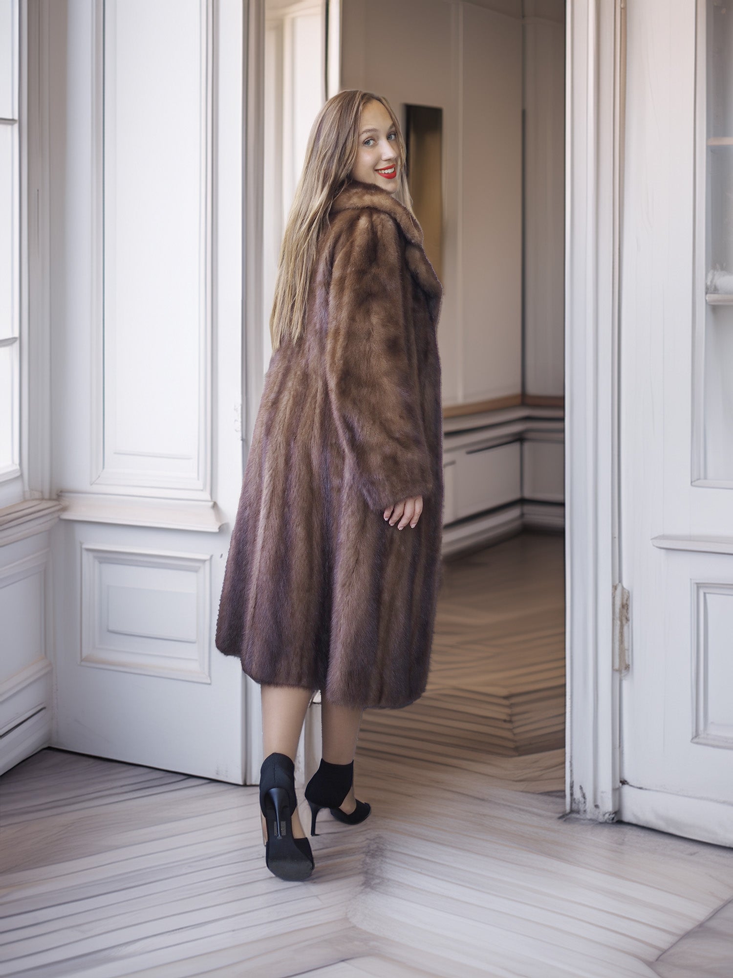 Woman wearing a brown fur coat standing in a room with white walls and wooden floor.