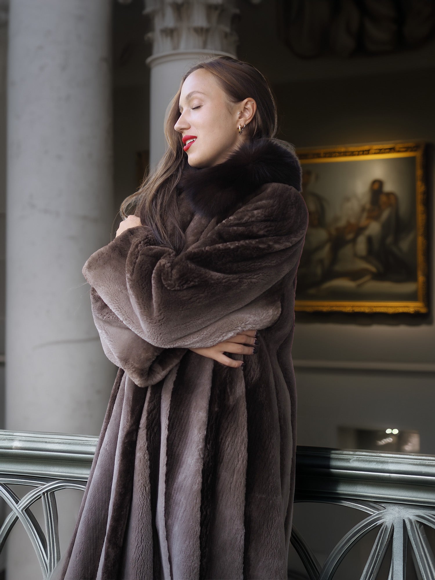Woman wearing a fur coat in an elegant interior setting with a painting in the background.