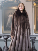 Woman wearing a long fur coat in an elegant interior setting with paintings on the wall.