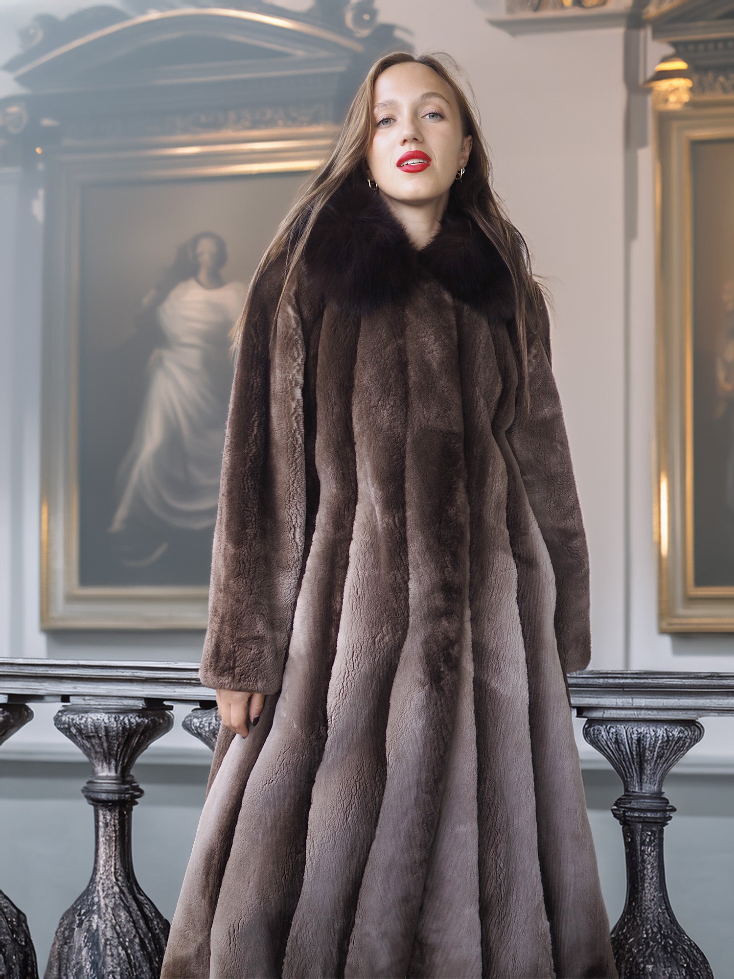 Woman wearing a long fur coat in an elegant interior setting with paintings on the wall.