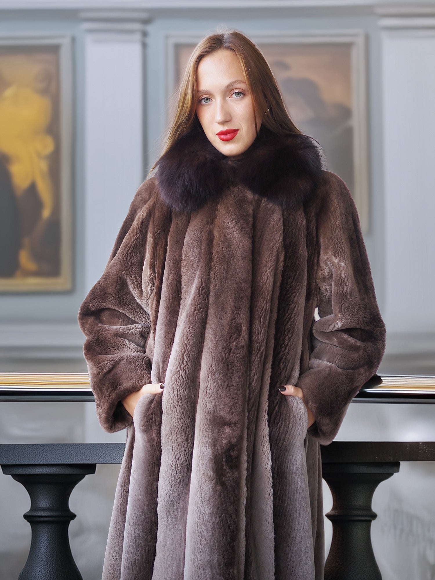 Woman wearing a long brown fur coat with a fur collar in an elegant interior setting.