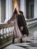 Woman in a long brown fur coat standing in an elegant hallway with columns.