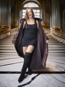 Woman in a long dark coat standing in an elegant interior setting