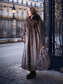 Woman in a fur coat standing in an elegant courtyard with classical architecture.