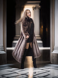Woman in a long brown coat standing in a grand hallway with columns.