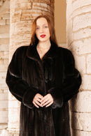 Woman wearing a dark fur coat standing against a stone wall.