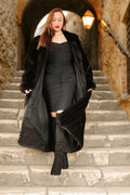 Woman in a long black coat standing on stone steps with a warm light in the background