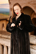 Woman wearing a black fur coat standing in front of an architectural structure.