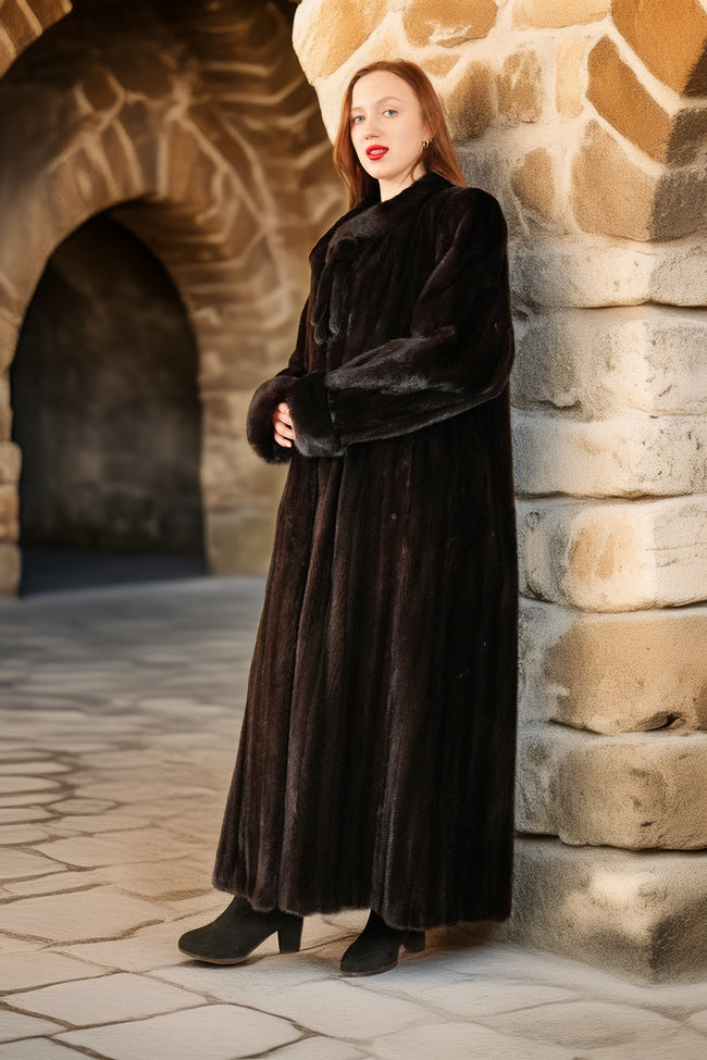 Woman in a long dark coat standing against a stone wall in an outdoor setting