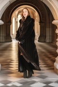 Woman in a long black coat standing in an elegant hallway with arched ceilings.