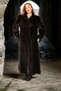 Woman wearing a long dark fur coat standing in a stone archway.