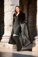 Woman in a long coat with fur trim standing in front of stone columns.