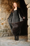 Woman in a long black coat standing in a stone archway.